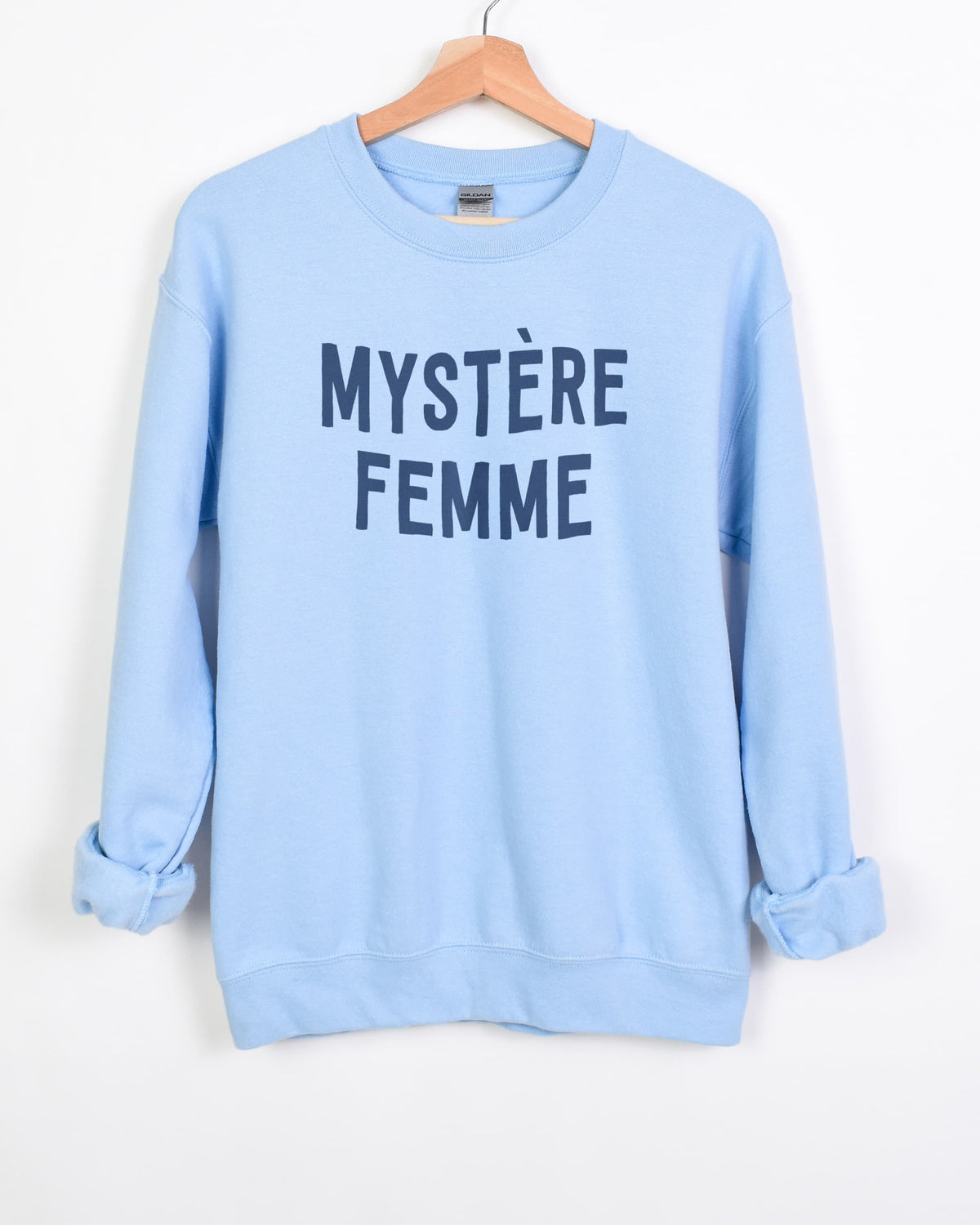 Mystère Femme sweatshirt in light blue with navy lettering on a hanger, sleeves rolled