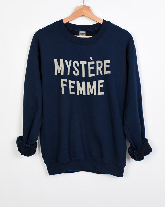 Mystère Femme sweatshirt in navy with cream lettering on a hanger, sleeves rolled to show the fleece lining